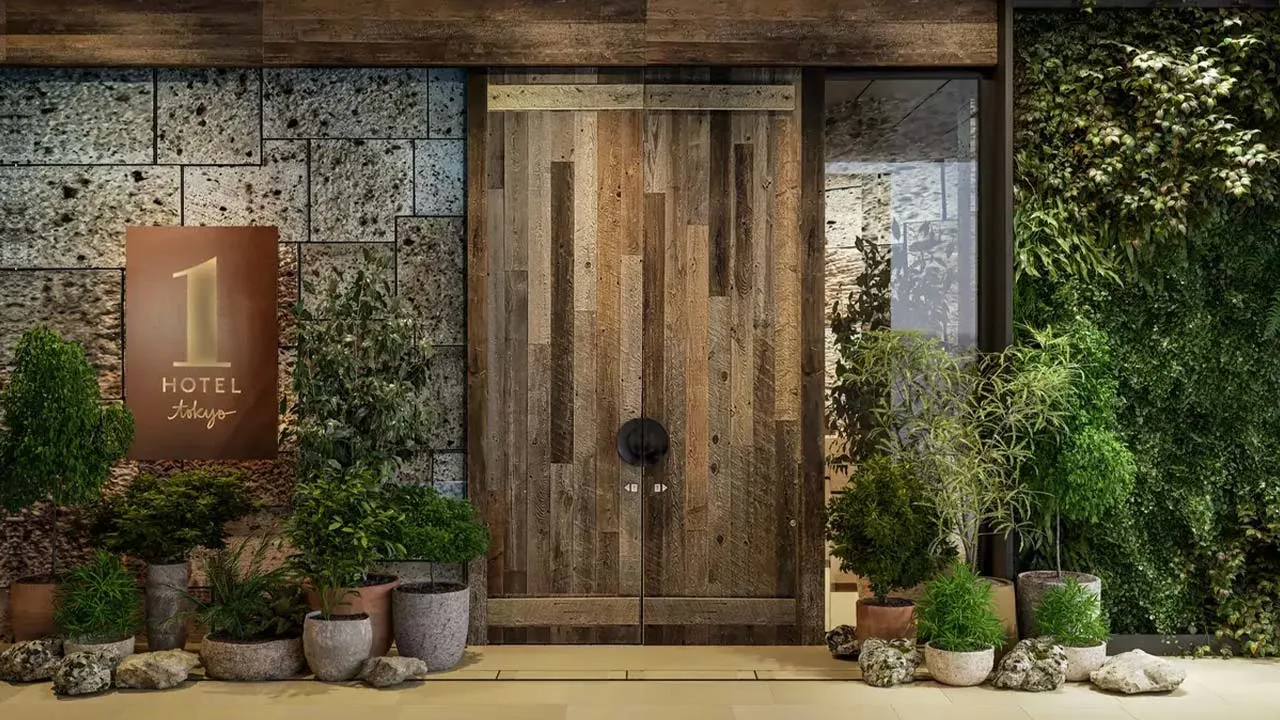 都会のオアシスへと誘う、1 Hotel Tokyo(ワンホテルトウキョウ)の重厚な木製エントランスドア。豊かなボタニカルウォールに迎えられ、日常を忘れる癒やしの空間へ。