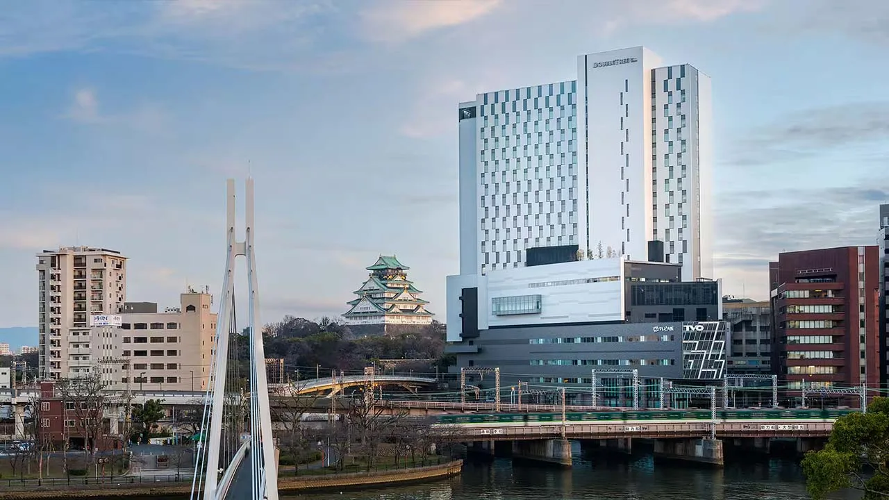 川や橋、電車が走る街の風景と並ぶダブルツリーbyヒルトン大阪城の外観および大阪城の遠景