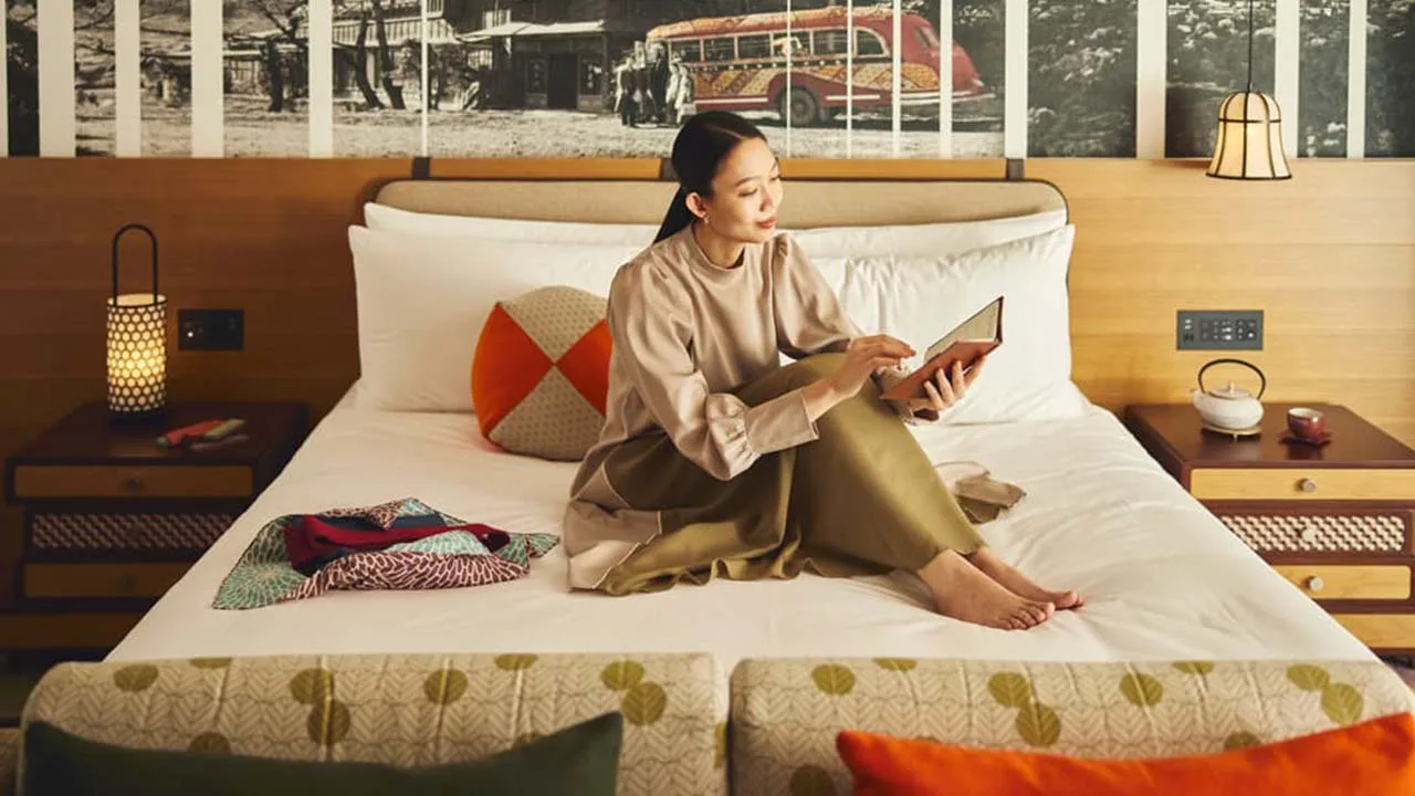 ホテルインディゴ箱根強羅のおしゃれでふかふかなベッドに腰掛け、読書をしながら自分へのご褒美のようなおこもり時間を満喫する女性