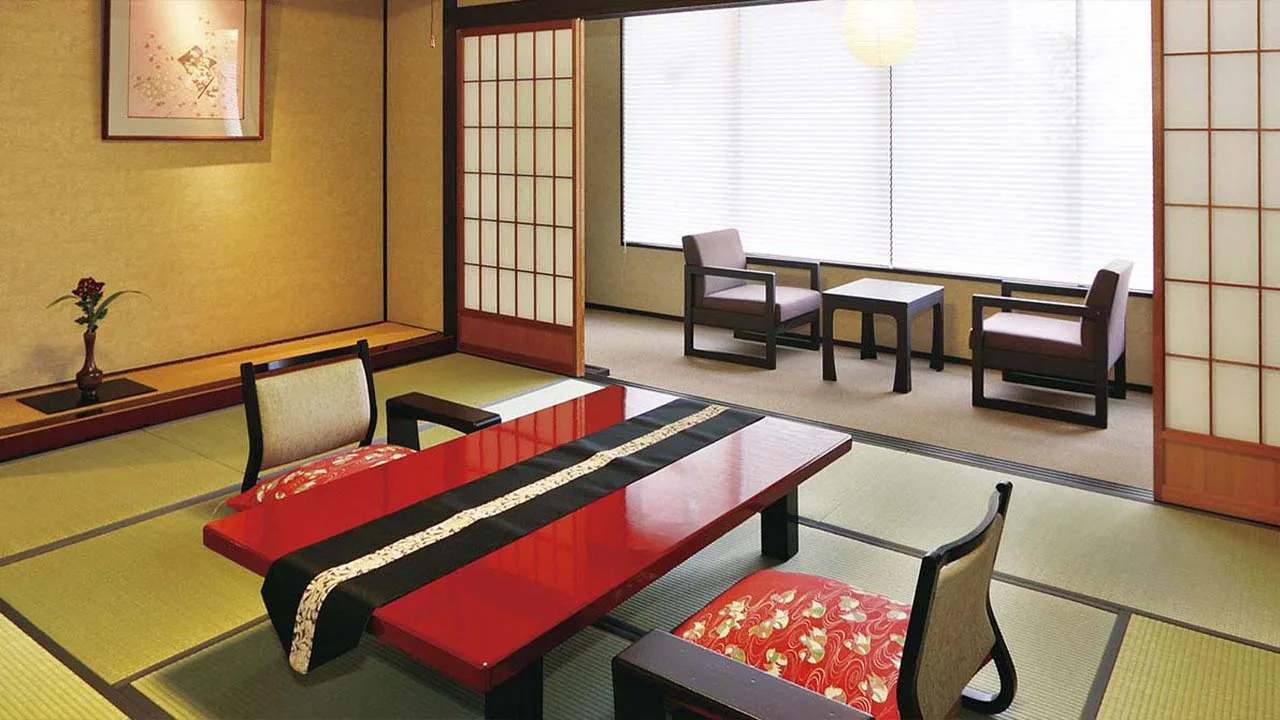 窓辺の椅子でゆったりと語り合える料理旅館 金沢茶屋の客室。洗練された和の設えと艶やかな朱色のテーブルが非日常のひとときを演出。