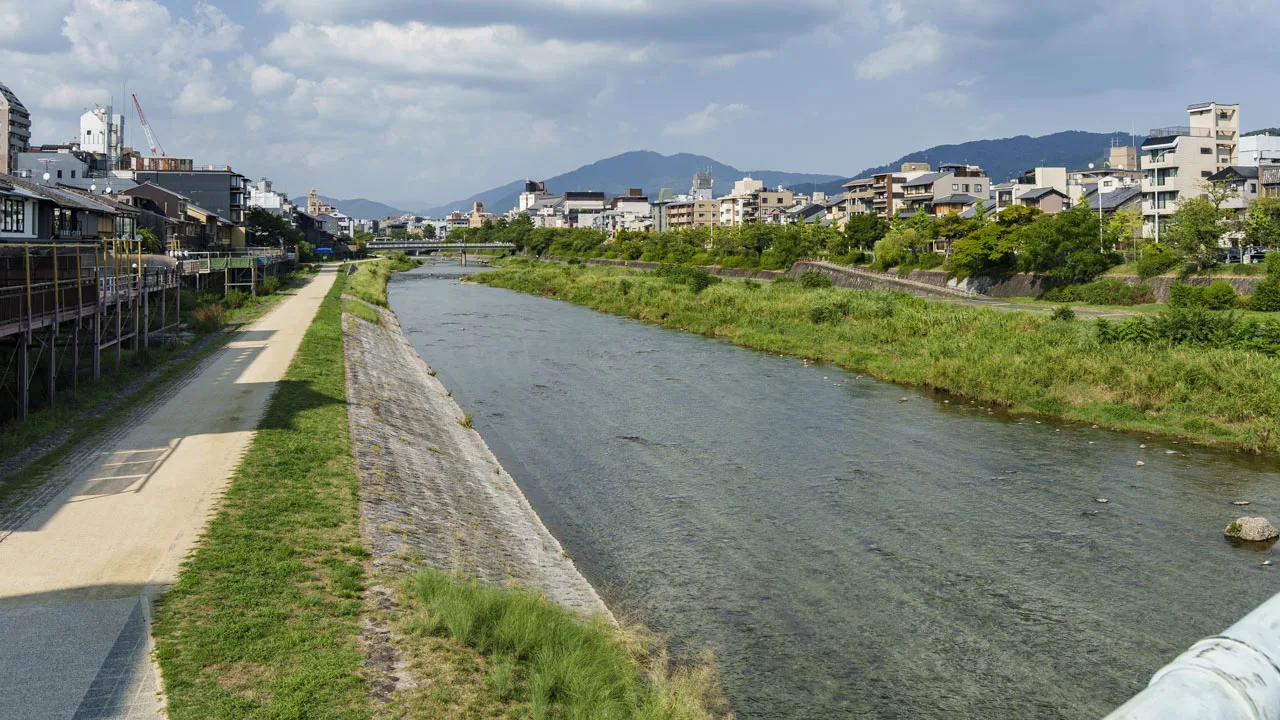 夏の青空の下、北に山並みを望む鴨川