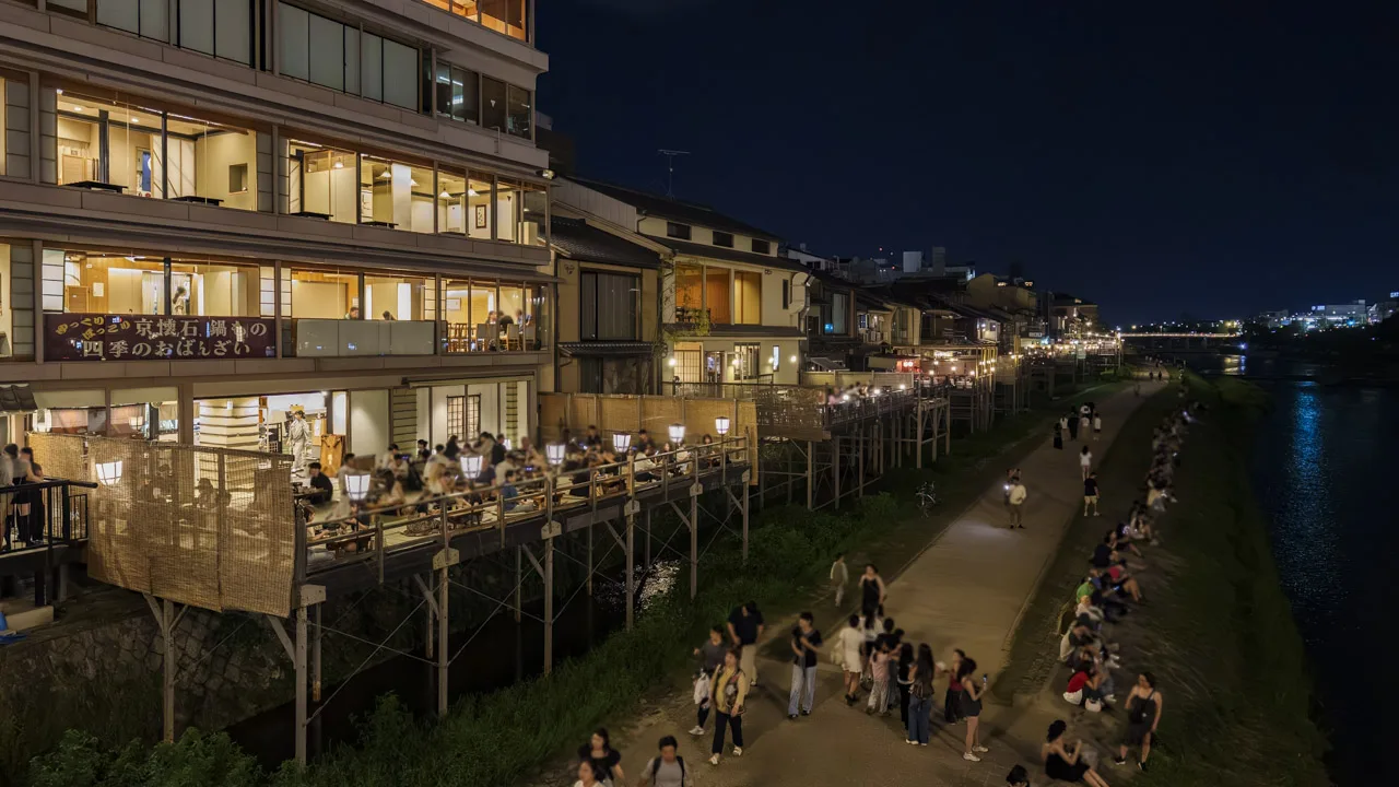 灯りがともった夜の納涼床と、川べりを歩く人たち