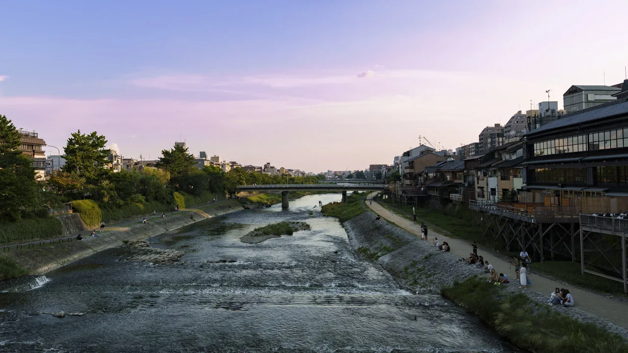 薄紫に染まる空と、西岸の川べりに座る人たち