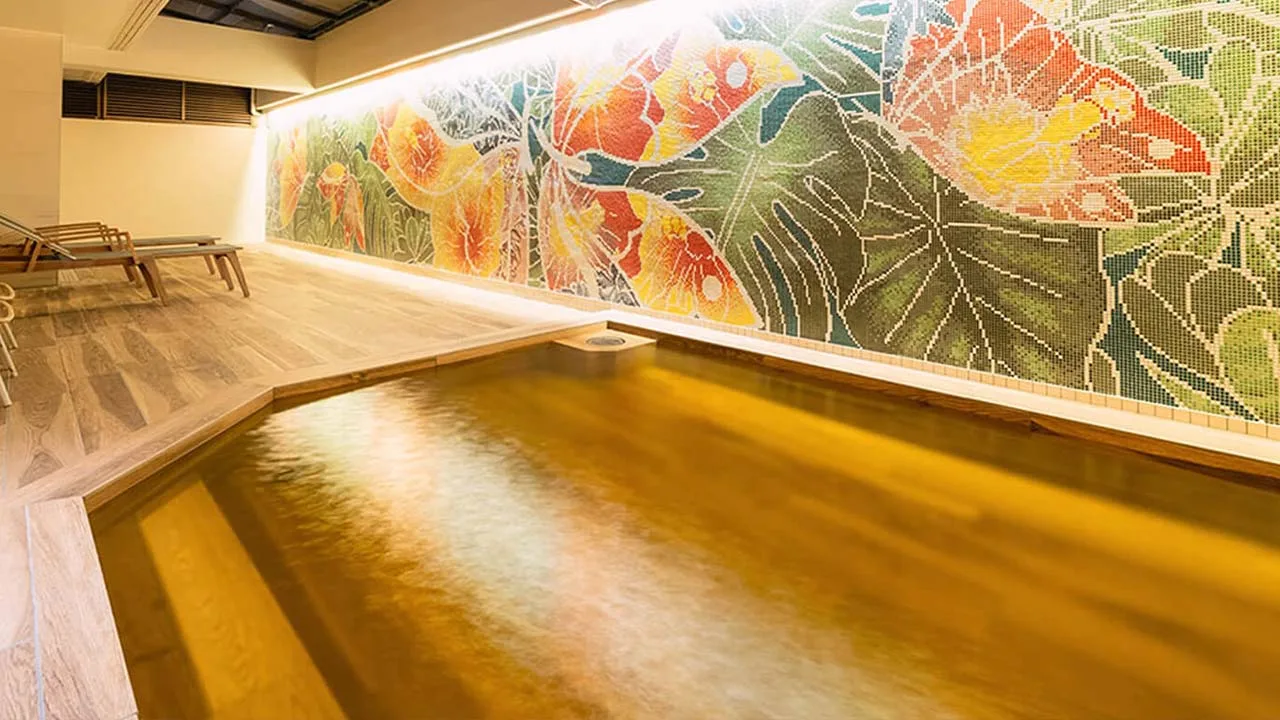 ロワジールホテル 那覇の天然温泉。壁一面に広がる南国花の鮮やかなモザイクアートにうっとりしながら、日常の疲れを芯から癒す至福のバスタイム。
