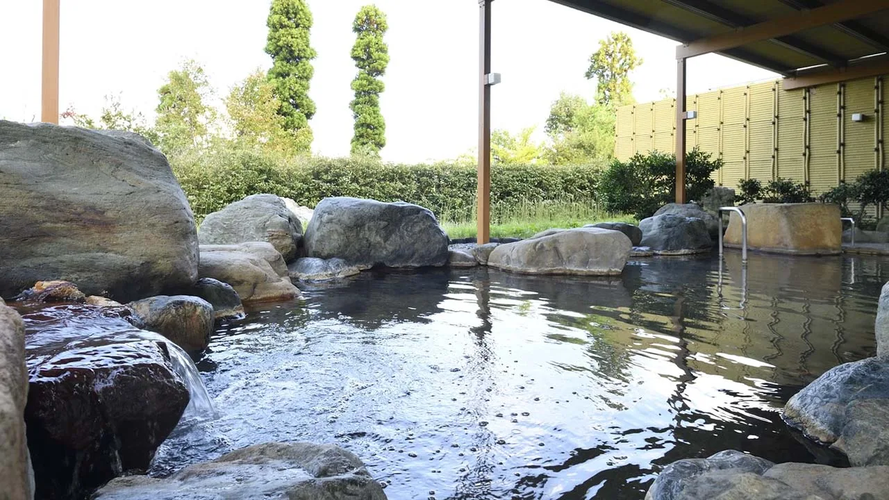 澄み切った青空と心地よい湯の音に包まれて至福のひとときを過ごすメルキュール富山砺波リゾート&スパの岩造りの露天風呂