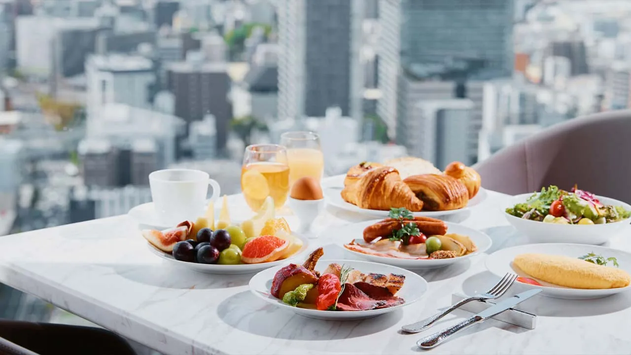 大阪ステーションホテルの絶景を背景に楽しむ優雅な朝食。焼きたてのクロワッサンや色鮮やかなフルーツが並ぶ、一日の始まりを彩る心ときめくモーニングタイム